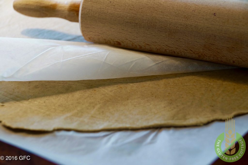 The strudle dough is rolled out between two parchment papers (gluten-free apple strudel).